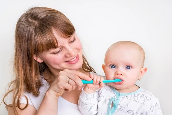 Mãe escovando os dentes de um bebê, introduzindo cuidados de higiene bucal desde a primeira infância para promover a saúde oral.