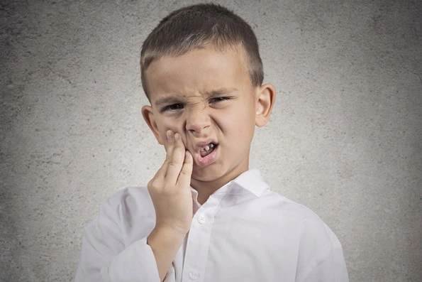 Criança com expressão de dor segurando o rosto, possivelmente devido a cárie ou trauma dental, ilustrando a necessidade de restauração dentária para aliviar a dor e recuperar a função do dente.